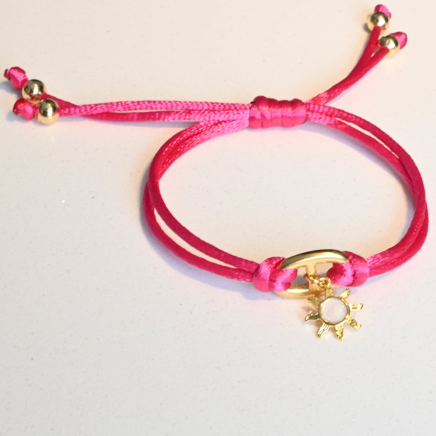 Pink bracelet with a gold charm on a light gray background